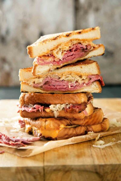 A stack of halved reuben sandwiches on a wooden cutting board.