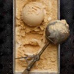 Salted caramel ice cream in a loaf pan on a pattern baking sheet with a scoop and scooper on top.