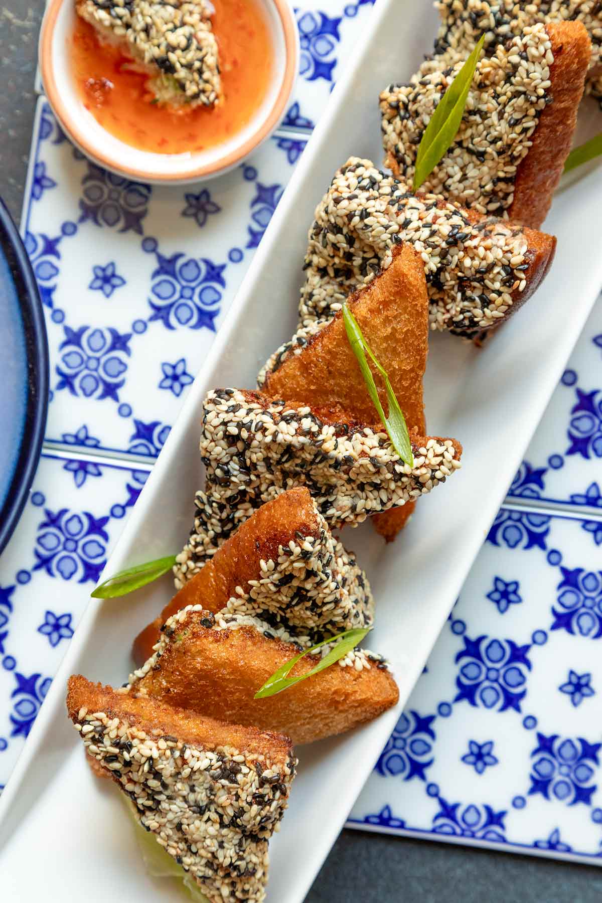 A rectangular platter of shrimp toast on top of blue and white tiles with a bowl of sweet and sour sauce on the side.