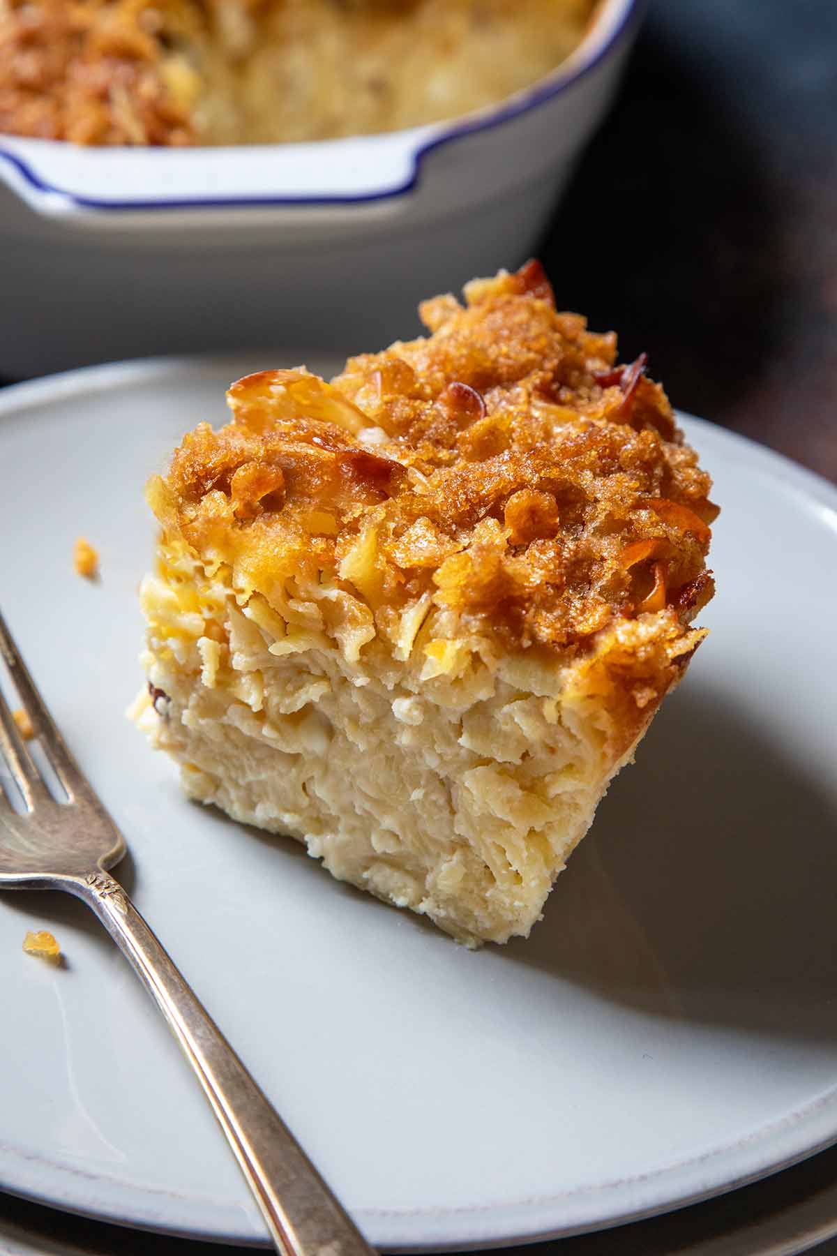 A casserole dish of sweet noodle kugel; in front is a plate with a slice of kugel on it.