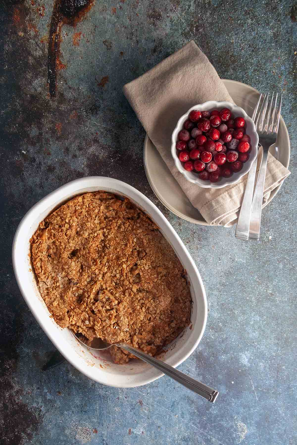 A whole apple cranberry crisp with a serving spoon resting inside.