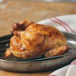 A trussed classic roast chicken on a rack, set inside a skillet.