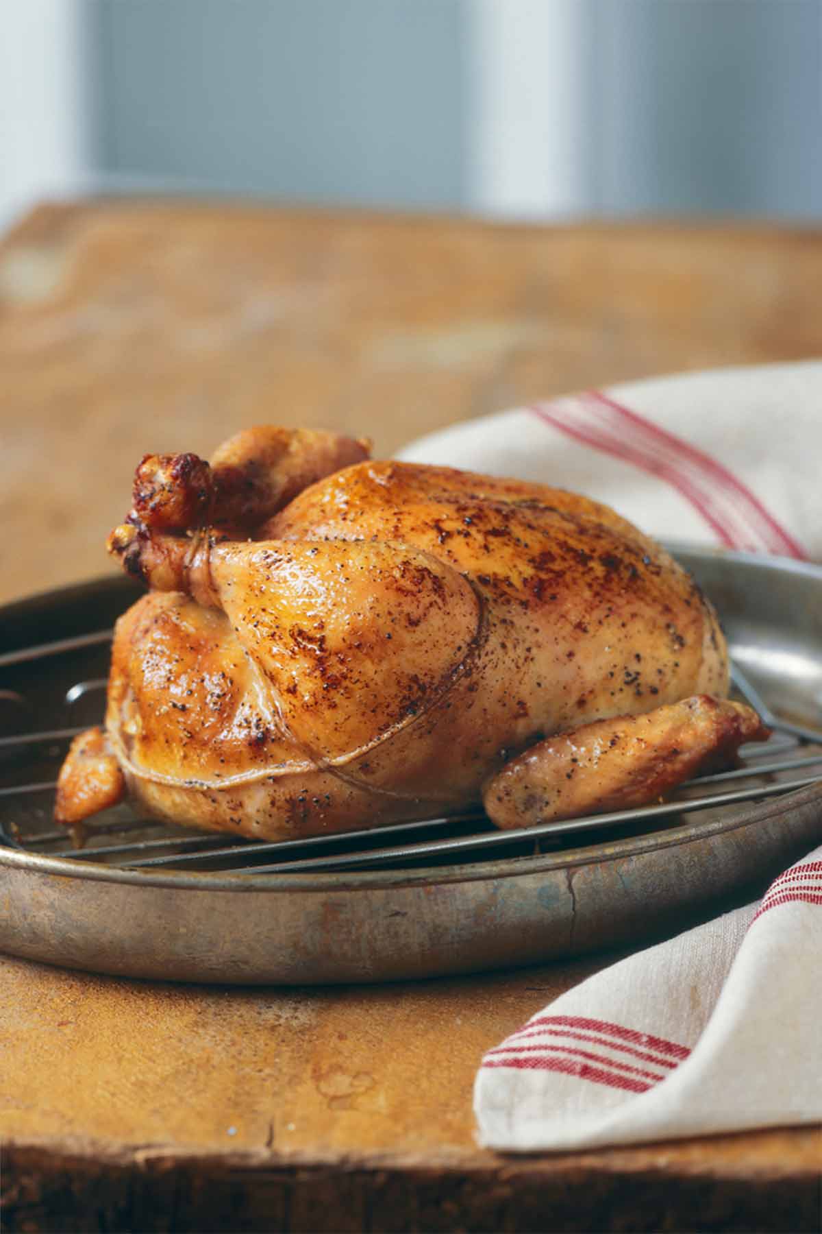 A trussed classic roast chicken on a rack, set inside a skillet.