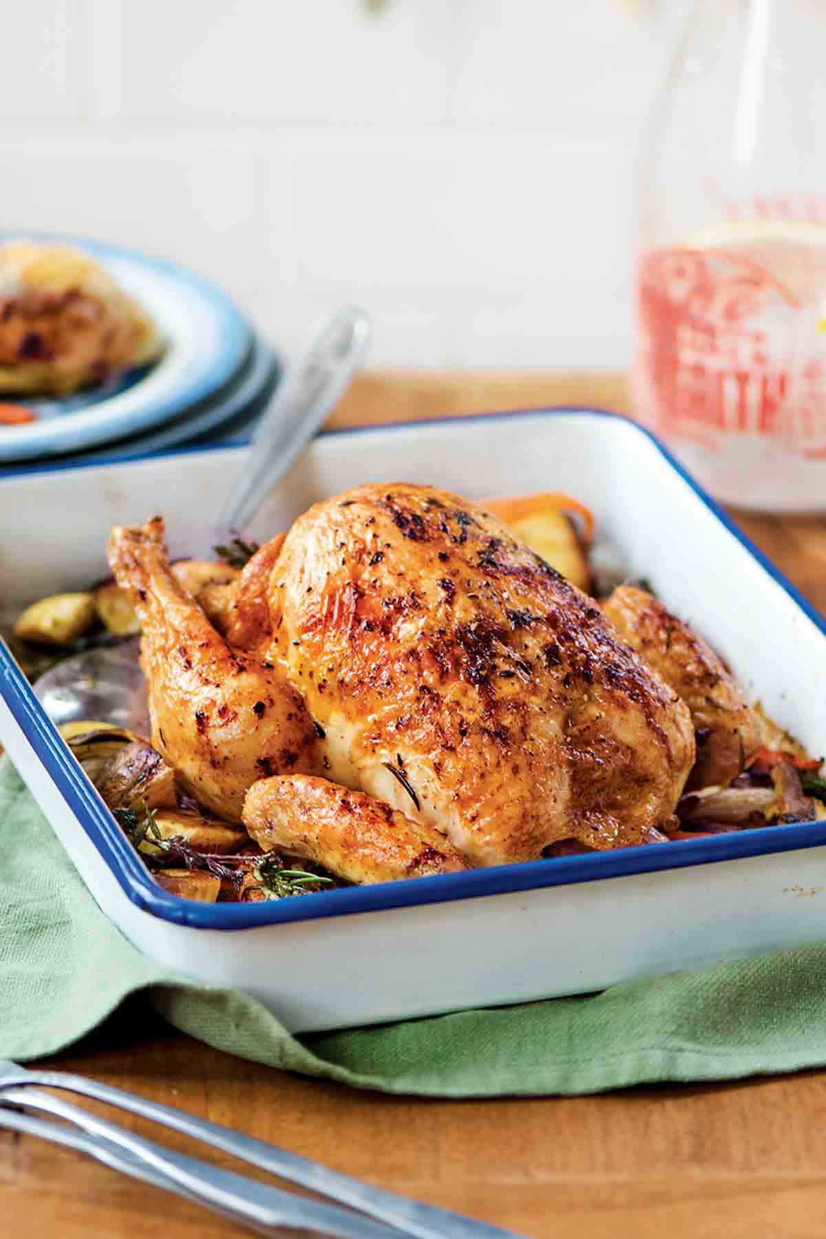 French roast chicken, called poulet rôti in French, in a white pan sitting top of roasted root vegetables.