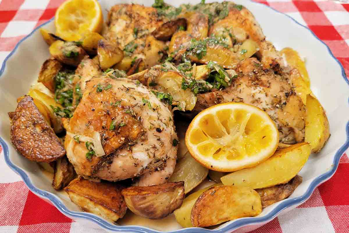 Chicken thighs, potatoes wedges and squeezed lemon halves on a white and blue platter.