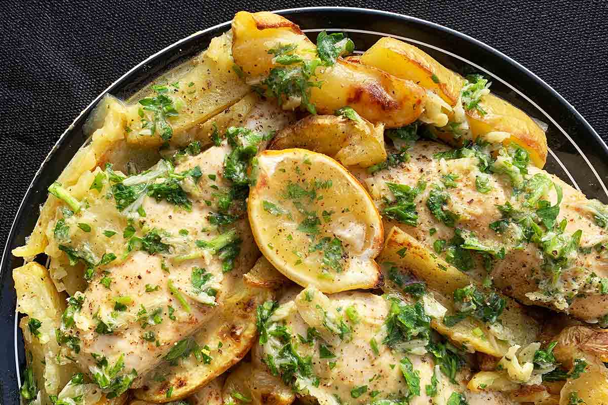 Chicken and potato pieces topped with parsley sauce and lemon wedges.