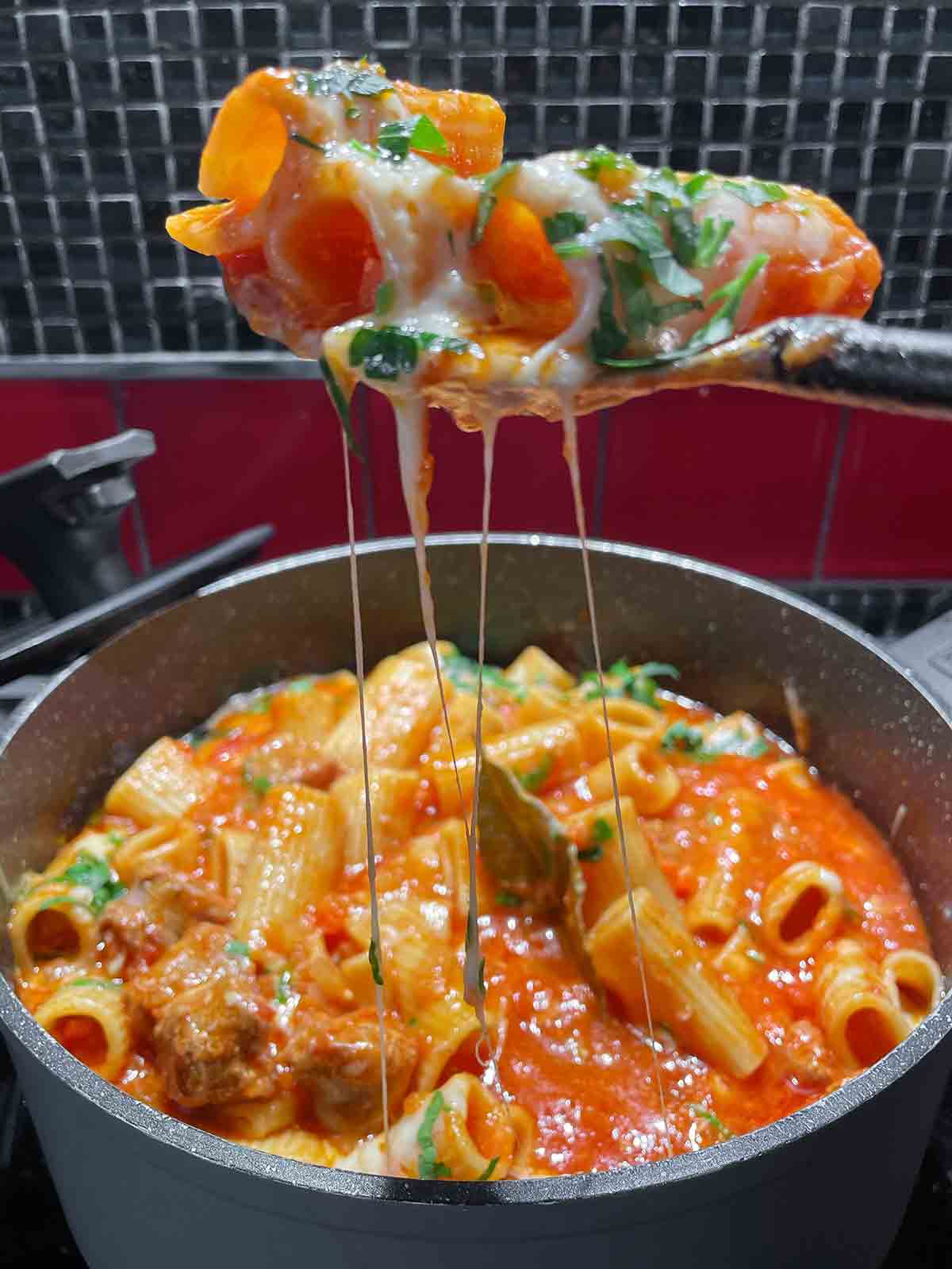 A scoop of pasta and tomato sauce being lifted from a pot.