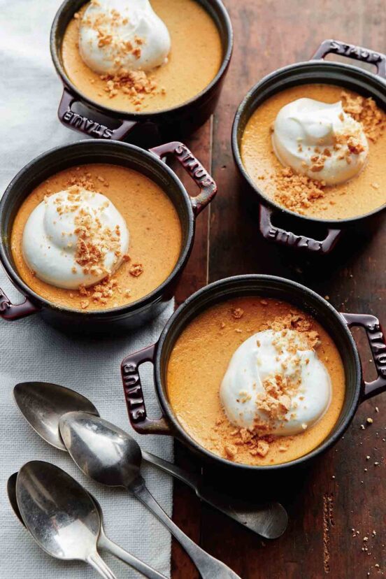 Four small crocks of pumpkin pots de creme--pumpkin pudding topped with crumbled cookie and whipped cream.