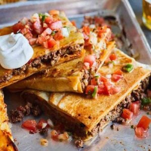 A cut sheet pan taco bake in a rimmed sheet pan topped with pico de gallo and sour cream.