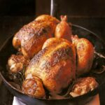 Two whole chickens and whole garlic heads in a cast iron pan.
