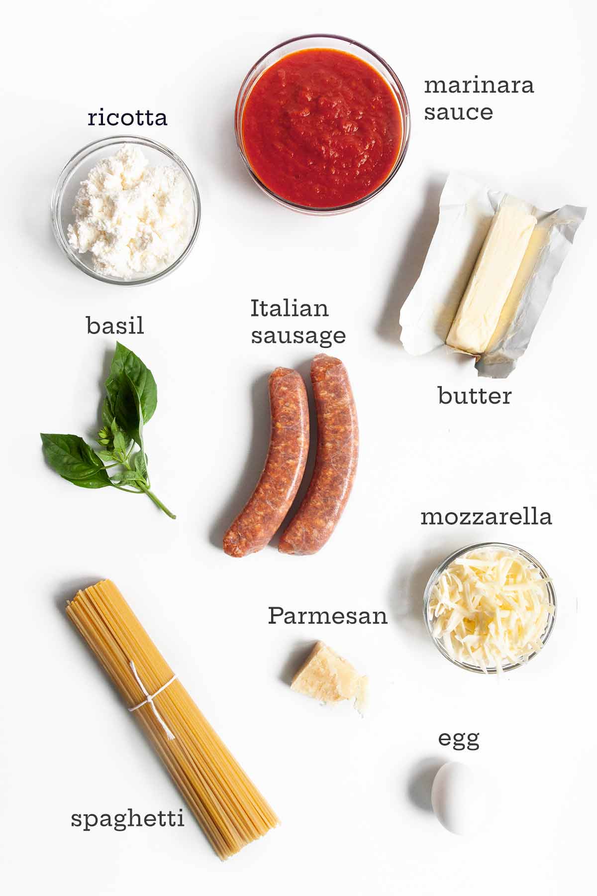 Ingredients for spaghetti pie--marinara, ricotta, sausage, butter, cheese, basil, spaghetti, and an egg.