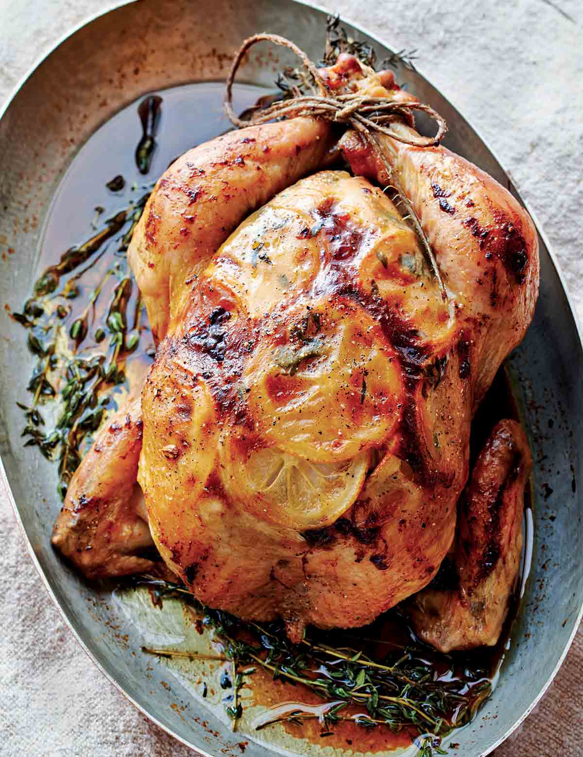 A whole roast chicken in an oval metal dish with fresh thyme scattered around it.