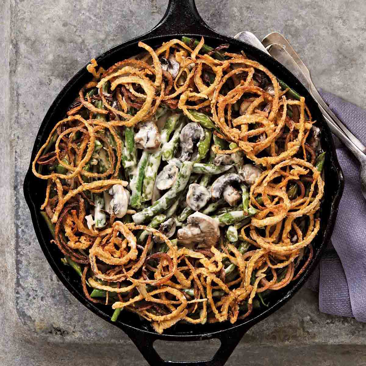 A classic green bean casserole with mushrooms and topped with fried onion rings in a cast-iron skillet.