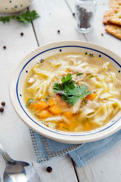 A bowl of chicken soup with carrots and noodles on a white table.