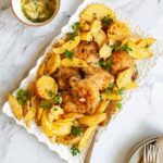 A platter filled with lemon-garlic chicken thighs, potato wedges, and lemon halves, and garnished with parsley sprigs.