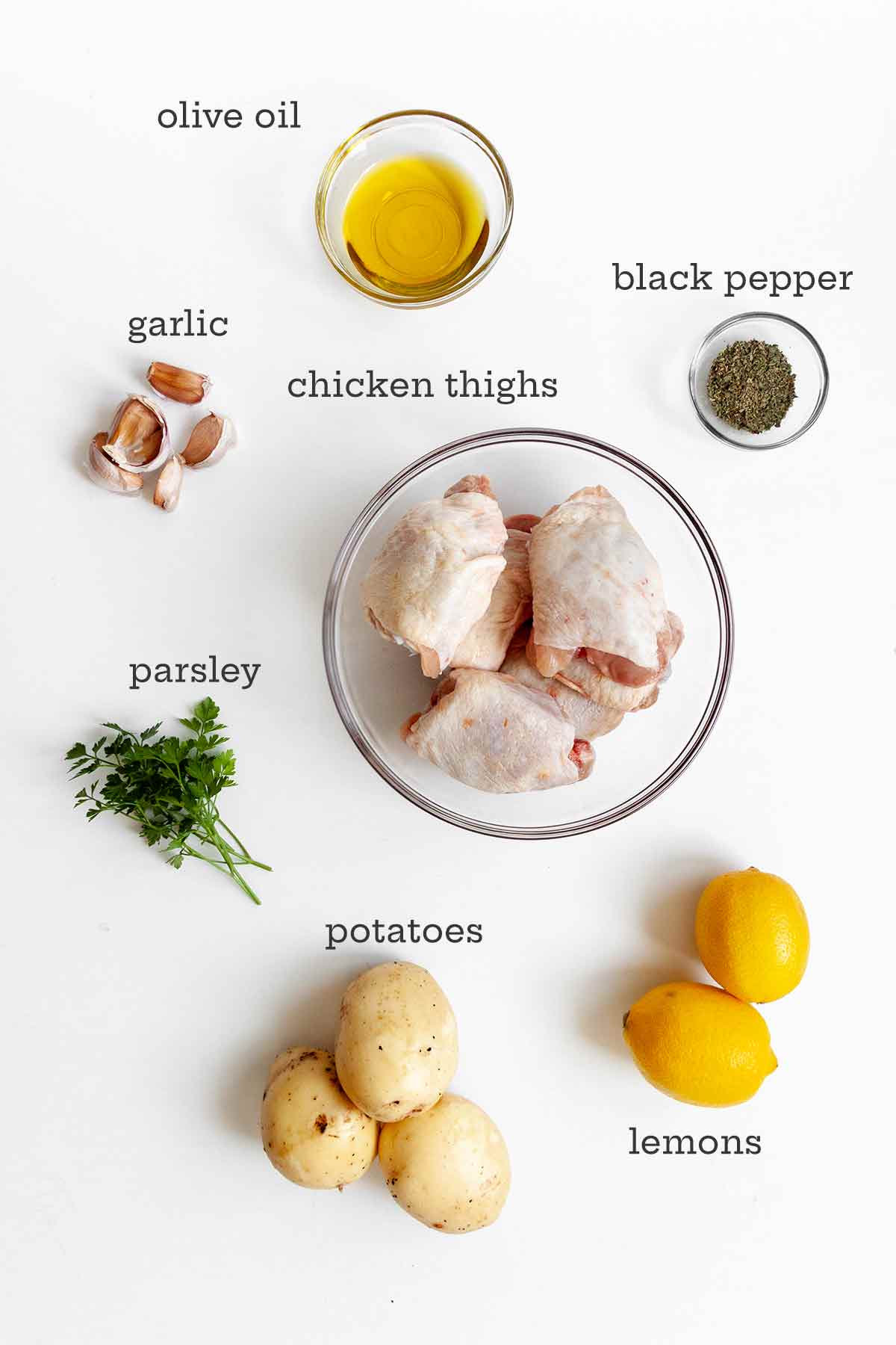 Ingredients for lemon-garlic sheet pan chicken thighs--chicken thighs, oil, pepper, garlic, parsley, potatoes, and lemon.