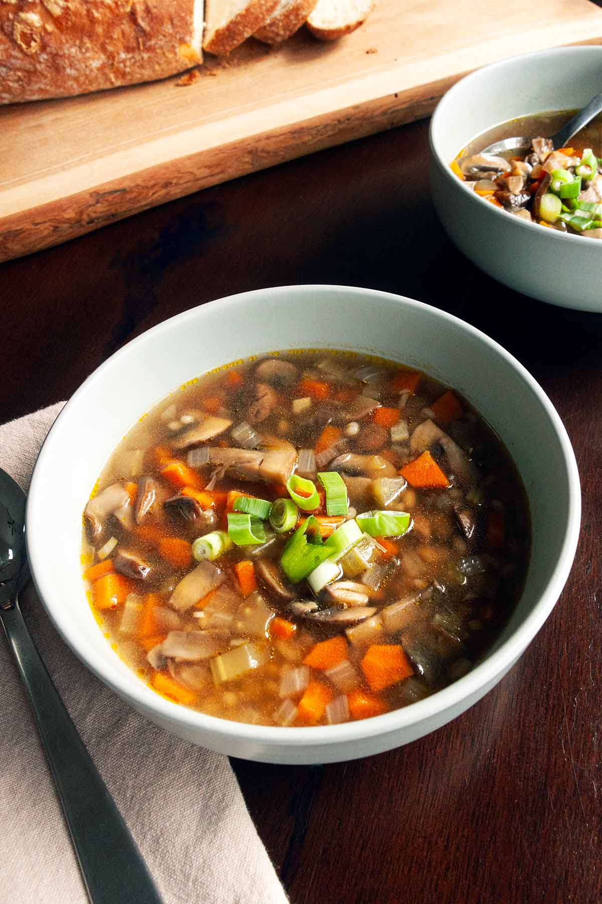 Two bowls of mushroom barley soup topped with sliced scallions on a table.