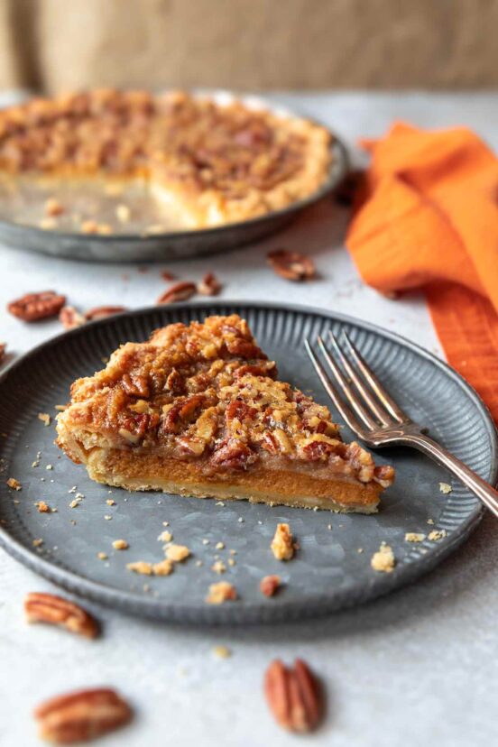 A slice of pumpkin pecan pie on a plate with the remainder of the pie in the background.