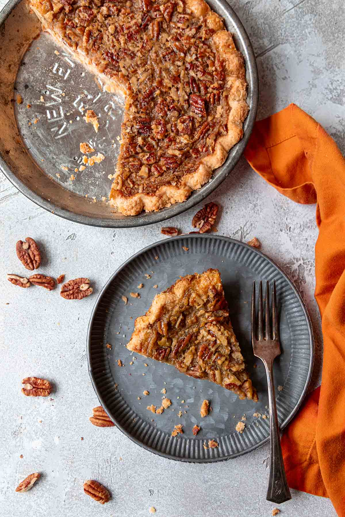 A slice of pumpkin pecan pie on a plate next to a pie plate filled with the remaining pie.