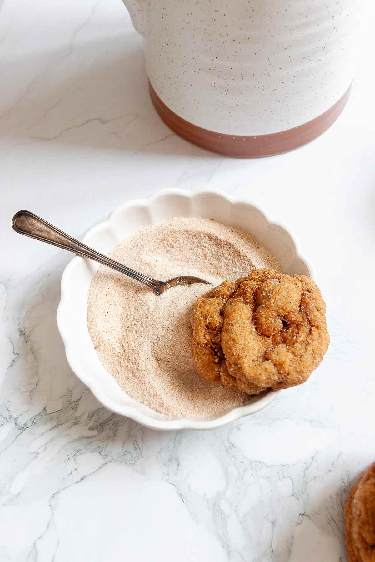 A pumpkin spice cookie resting on the edge of a bowl of spiced sugar.