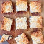 A slab of pumpkin spice seven layer bars cut into ten pieces on a wooden board.
