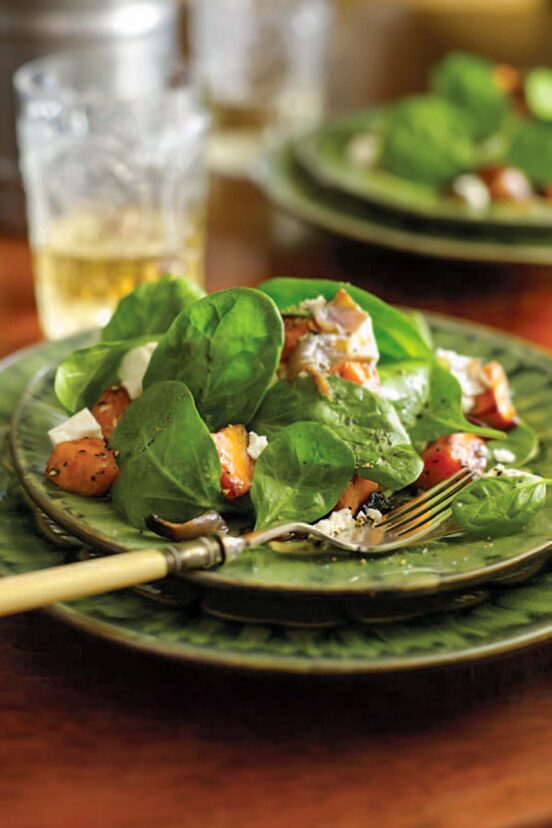A serving of roasted sweet potato and feta salad on a green plate with a fork resting on the plate.