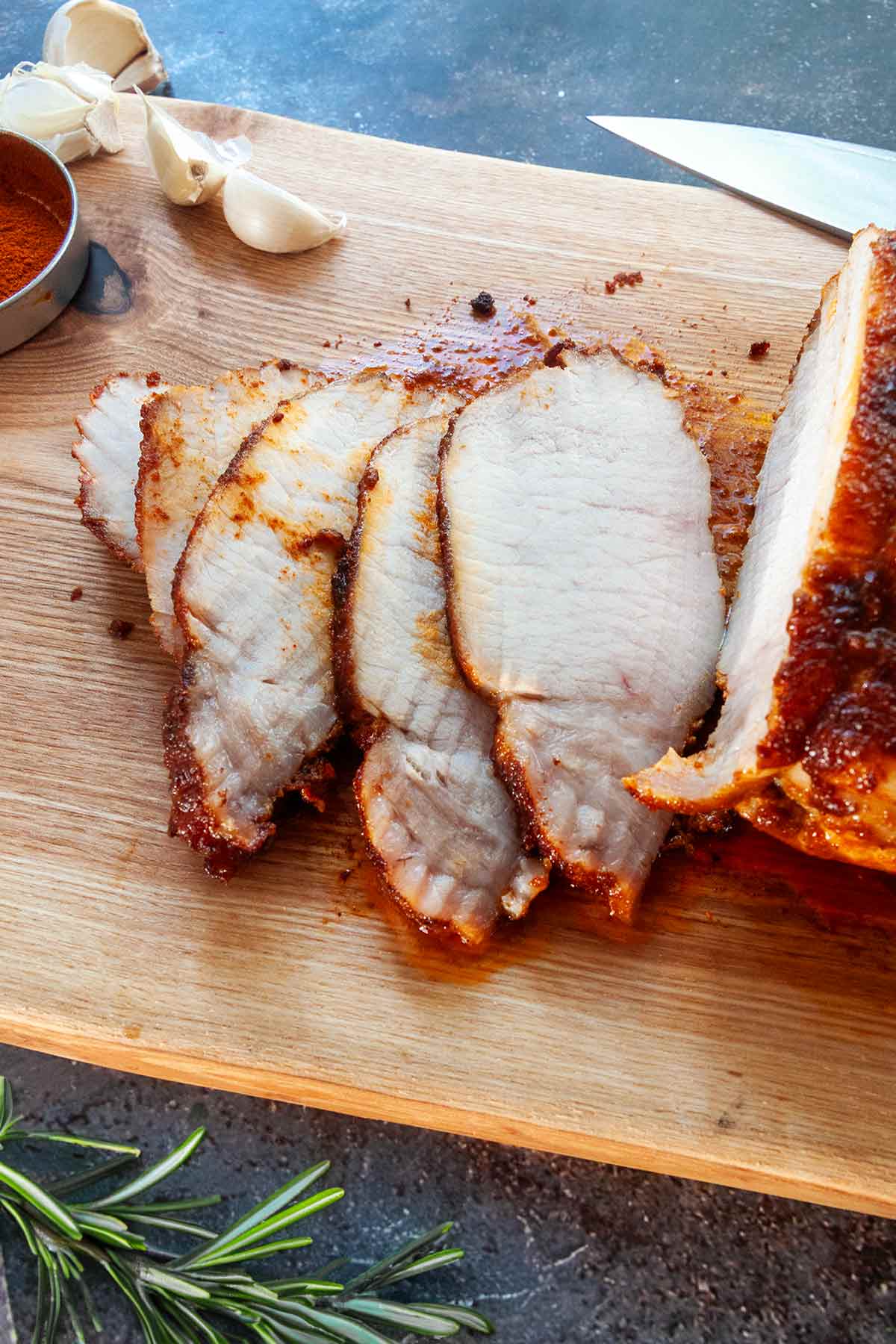 A partially sliced pork loin roast on a cutting board with garlic and paprika.