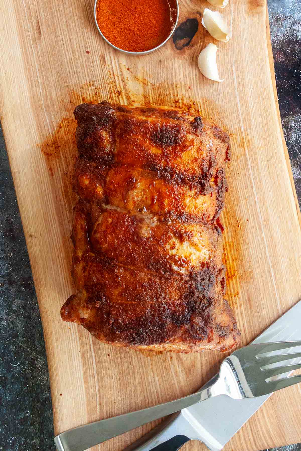 A Spanish pork loin roast on a cutting board with a carving knife and fork next to it.