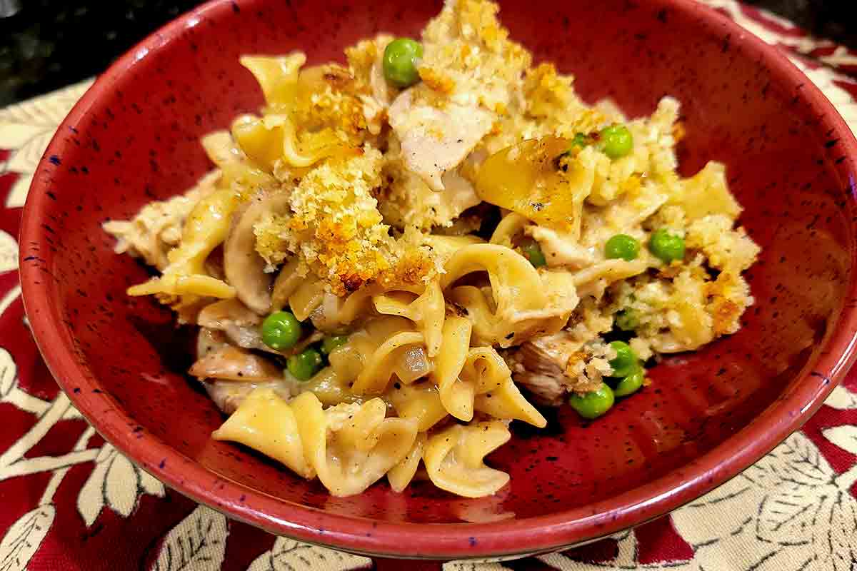 A red bowl filled with turkey tetrazzini with a crispy browned topping.
