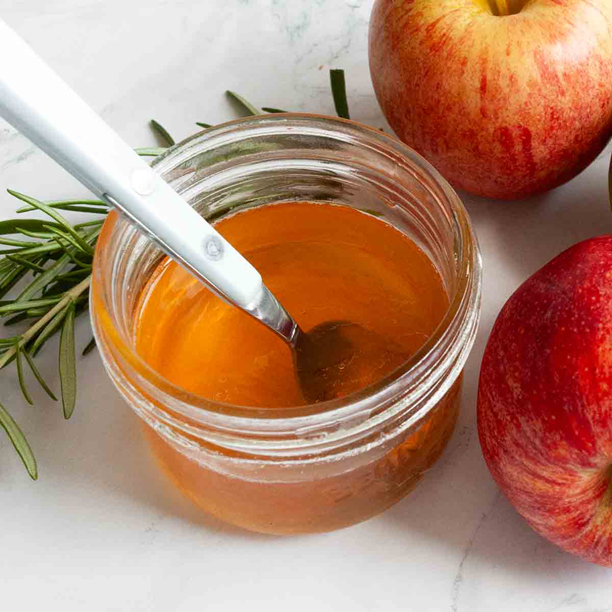 A small jar of apple jelly with a spoon in it.