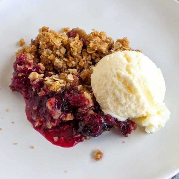 A portion of blueberry crumble on a white plate with a scoop of vanilla ice cream on the side.