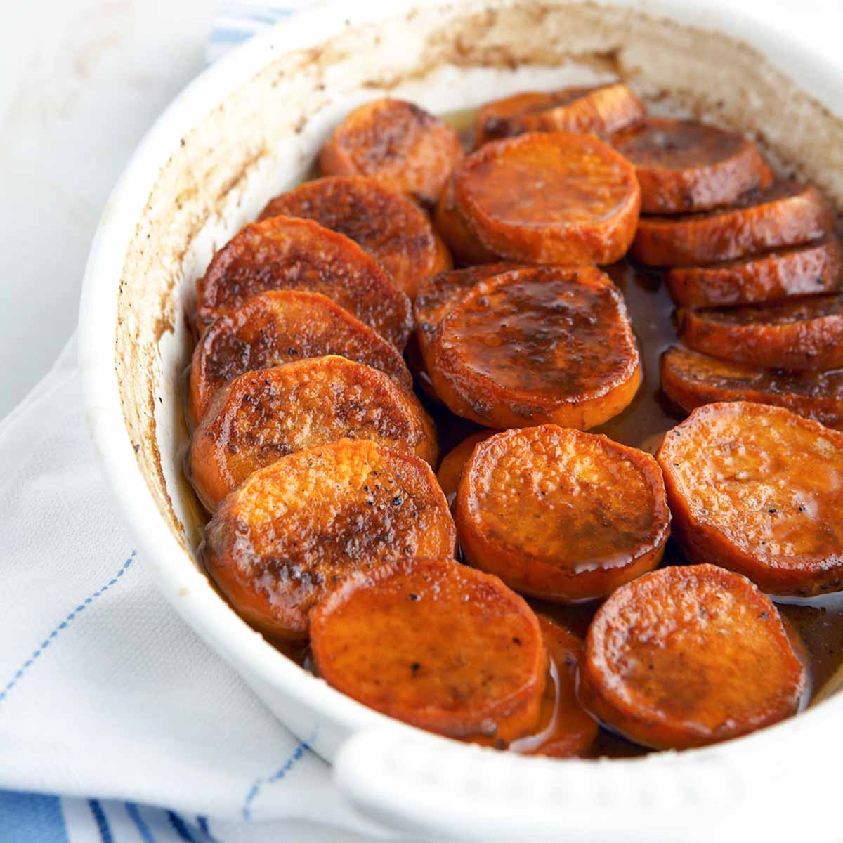 Bourbon sweet potatoes in a white oval baking dish, sitting on a white and blue tea towel.