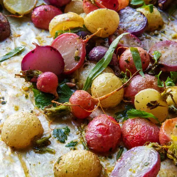 A tray of oven-roasted radishes with parsley and tarragon leaves.