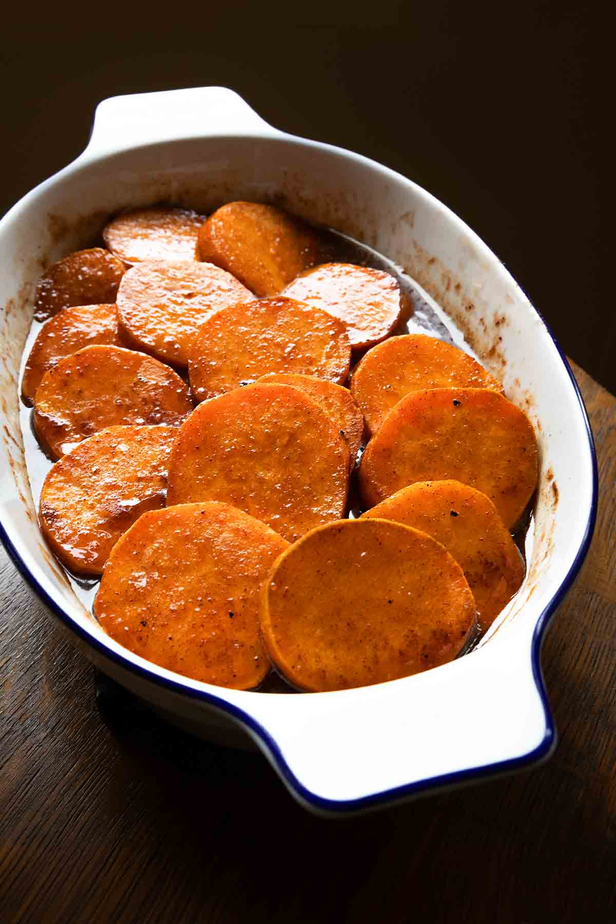 An oval baking dish filled with slices of candied sweet potatoes in a brown sugar syrup.
