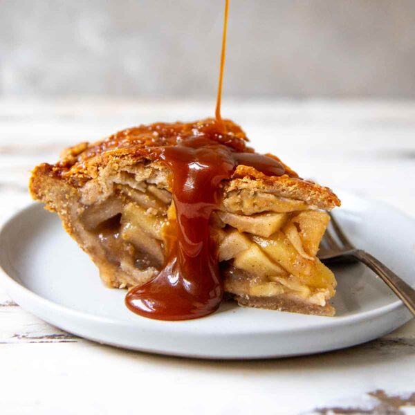 Caramel sauce drizzled over a slice of apple pie on a white plate.