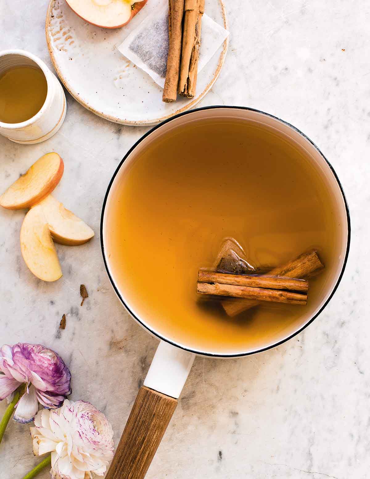A white enamel pot filled with chai spiced apple cider and two cinnamon sticks.
