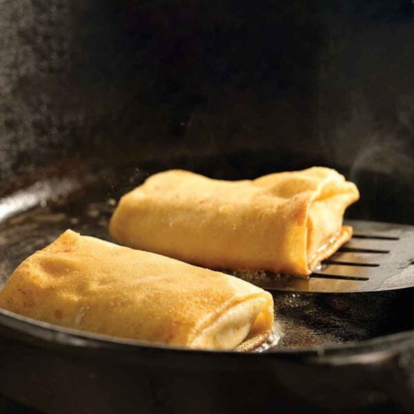 Cheese blintzes in a cast-iron frying pan, one being lifted up by a metal spatula.