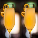 Two glasses of orange-colored Christmas cocktail with orange twists on the glasses.