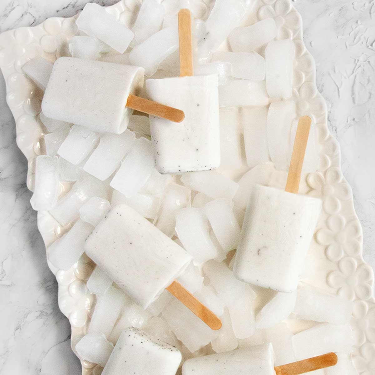 Six coconut milk popsicles on a platter filled with ice.