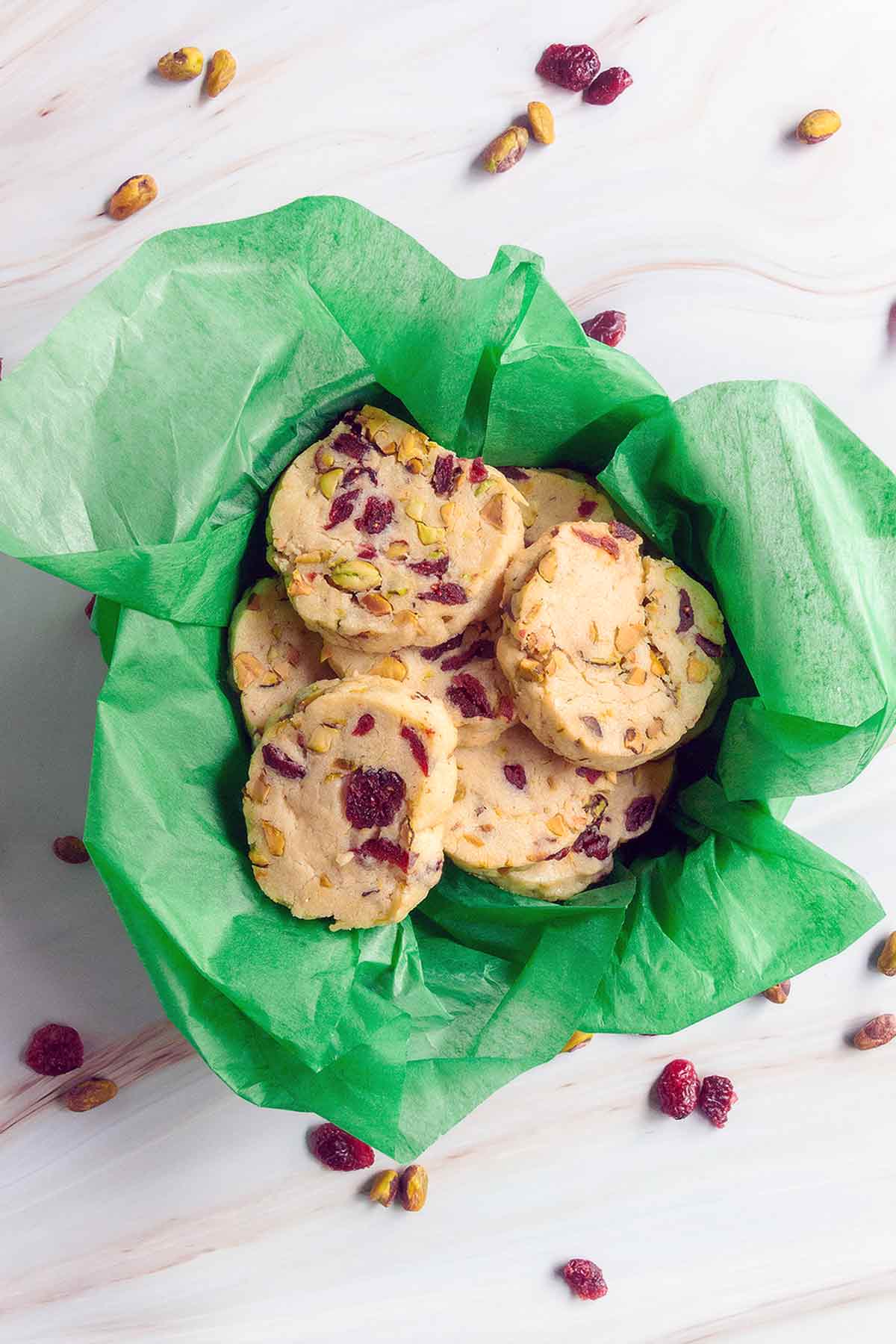 Cranberry pistachio cookies in a cookie tin lined with green tissue paper.