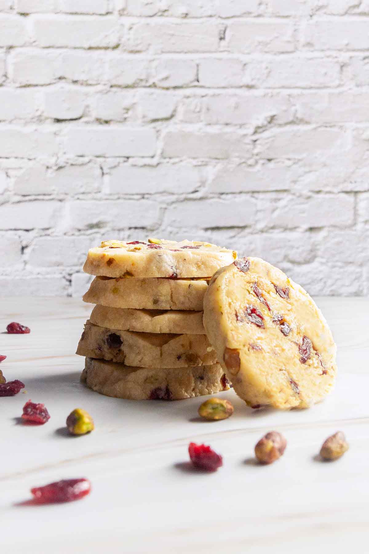 Five stacked cranberry pistachio cookies with another cookie leaning against the stack.
