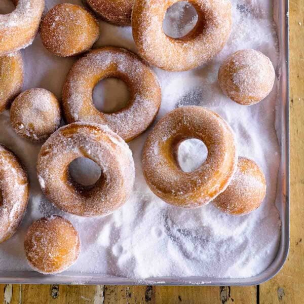 Easy Jewish Hanukkah doughnuts and doughnut holes covered with sugar, on a metal cookie sheet.