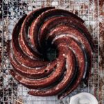 A swirled gingerbread Bundt cake with a lemon glaze on top, all on wire rack over a sheet pan.