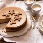 A whole gingerbread cheesecake on a white platter with a slice missing from it.