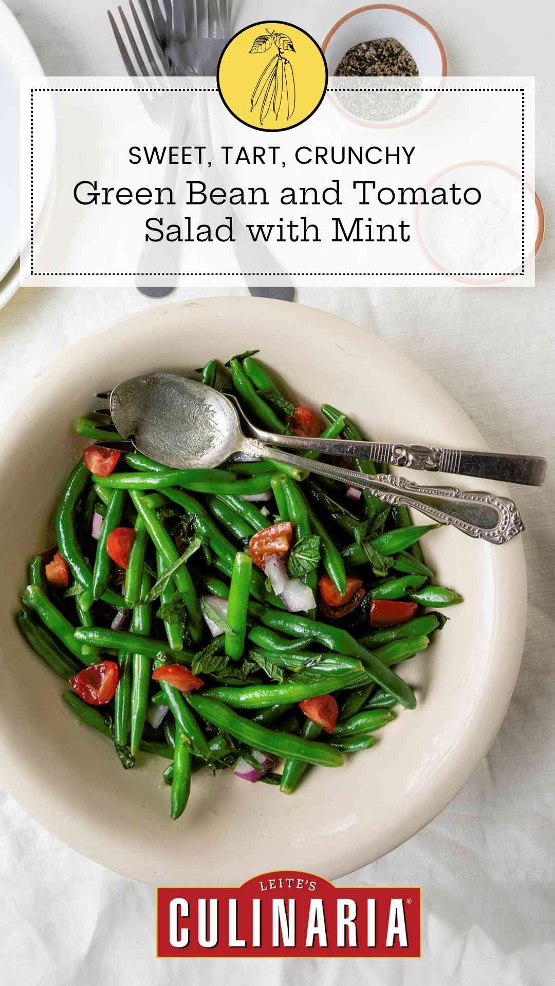 A bowl of green bean salad with mint and tomatoes with a serving spoon and fork resting on top.