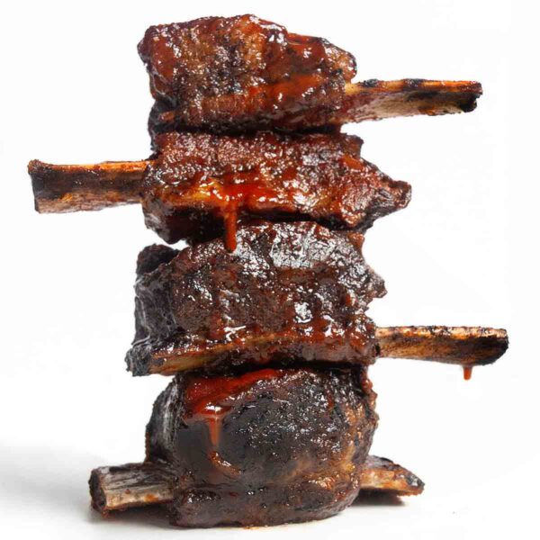 Four grilled short ribs in a stack on a white background.