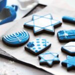 A selection of frosted cookies decorated for Hanukkah, on a parchment-lined cookie sheet.