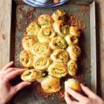 Jamie Oliver's Garlic Pull-Apart Rolls on a metal sheet pan, garnished with crispy bread crumbs, and being pulled apart by two hands.