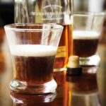 Two glasses half-filled with Kentucky coffee and an open bottle of bourbon between them.