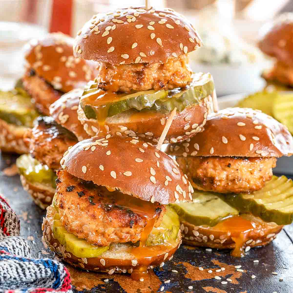 Nashville hot chicken sliders, piled up on a plate with sesame seeds and hot sauce.